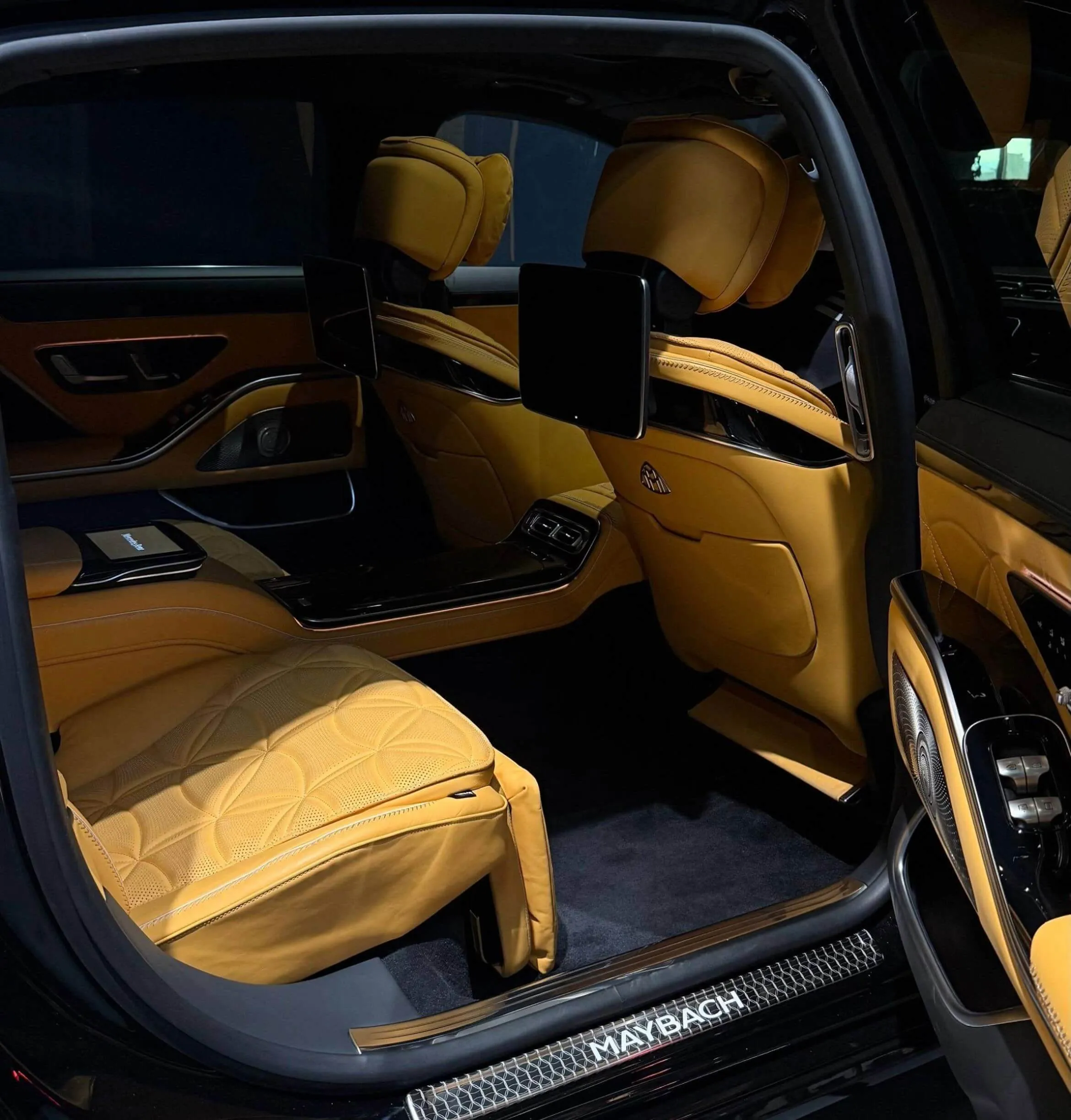 Luxurious tan leather rear seats and spacious cabin of a Maybach S-Class sedan with open door, showing entertainment screens and exquisite details.