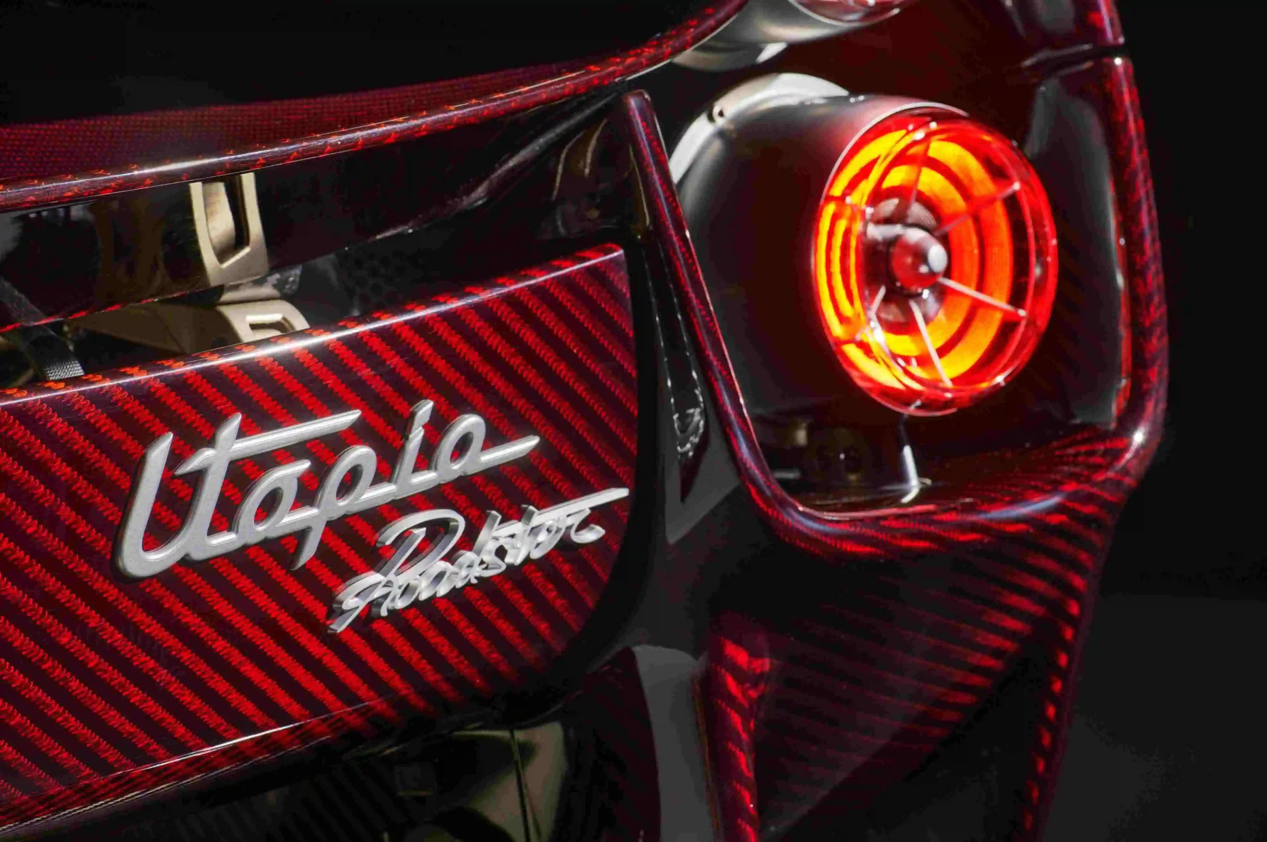 Close-up of the Pagani Utopia Roadster's glowing circular turbine taillight and the silver Utopia Roadster script on the red carbon-fiber body.